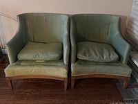 Front view of two vintage Barrymore mid century arm chairs with green fabric upholstery, worn condition, one missing bottom cushion and cover.