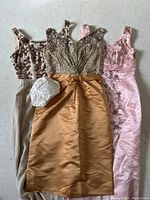 Top down view of the three beaded dresses and beaded Juliet cap hat, showing design details and colors