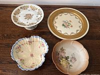Photo of vintage floral china including a white and gold cake stand, gold rimmed tray, scalloped shell-shaped bowl with chip, and round floral bowl