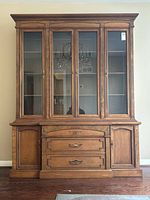 Front view of the vintage solid walnut china cabinet showing upper glass doors, interior shelves, three drawers, and side cabinet doors.