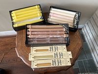 Three boxes of Concord wax taper candles in yellow, white, and brown, along with two packs of Ambiance dinner dinner taper candles on an octagonal wooden table.