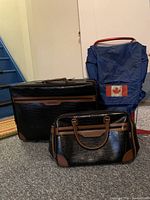 Full view of large faux leather suitcase, smaller matching bag, and blue canvas backpack with Canadian flag patch.