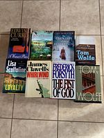 Top-down view of the eight assorted novels arranged on floor showing front covers including titles and authors.