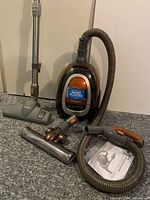 Overall view of Bissell vacuum cleaner with hose, wand, attachments, and manual set on the floor