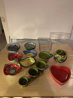 Full lot arranged on table showing colorful ceramic dipping dishes, measuring cups, heart-shaped dish, votive candleholder, and square glass vase