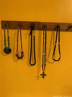 Six assorted necklaces hanging on wall hooks against yellow wall, showing variety of bead colors and styles
