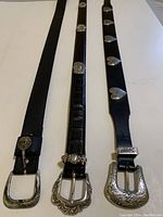 Three black ladies' belts side by side showing buckle ends with silver accents and different textures