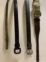 Four assorted ladies belts laid flat showing buckles and textures including leather and vinyl materials.