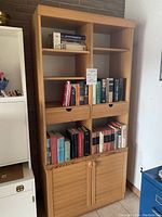 Full front view of the large wooden bookcase filled with books on the shelves, two drawers in middle section, and closed base cupboards.