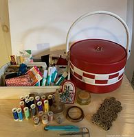 Photo of entire lot showing round red and white sewing box, extra tray with various sewing supplies spread out in front