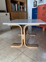Side view of the white square end table showing the wooden base with curved supports and the flat white top surface.