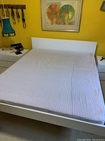 Queen size wood frame bed with mattress in a bedroom setting under a framed art piece, showing the bed assembled with mattress on top.