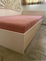 Side angle shot of the wood frame single bed with pink floral mattress cover in a bedroom.