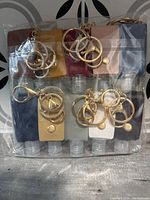 Set of 10 clear plastic hand sanitizer bottles, each inside different colored snap-button pouches with gold-tone metal purse clip keyrings attached.