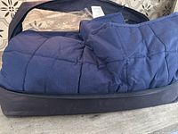 Close-up of a navy blue quilted weighted blanket partially inside a navy blue carry bag