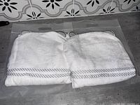 Two new white hooded towels in plastic packaging, folded, showing the striped border and ear details on hoods.