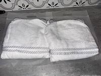 Two white organic bamboo hooded towels with striped border and ears, displayed side by side in packaging
