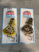Two new Rebel Buzz'N Frog fishing lures in yellow and black spotted frog design still in original packaging.