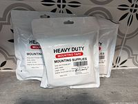 Three white sealed bags containing heavy duty mounting tape rolls, each labeled with product details like model, size, and material.