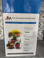 Box front showing images of six clear stackable fridge bins with sample fruits and vegetables inside, and text describing features: clear, organizes extra fridge or freezer space.