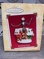 Front of box displaying the ornament of Jack Skellington standing between two snow-covered houses, with brand and character information.