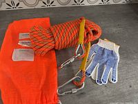 Full lot laid out showing the orange climbing rope coiled with metal carabiners attached, white textile gloves with blue grip dots, and orange nylon carry bag with labels.