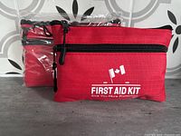 Photo of two red first aid kits, one sealed in plastic and one unpackaged, showing front with Canadian flag and text.