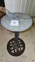 Full view of the cast iron sundial showing the dragonfly gnomon, dial plate with Roman numerals and inscription, and ornate circular base.