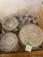 Photo showing a variety of crystal and glassware items arranged on a table including serving trays, bowls, stemware and glasses, all with cut and etched patterns.