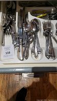 Top down view of mixed cutlery including knives, spoons, forks in a white plastic organizer tray.