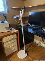 White and gray Dyson floor dock standing on wooden floor in room with computer desk and printer, showing full dock including base and vacuum holder section.