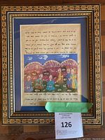 Framed illuminated page showing Hebrew script and watercolor banquet scene