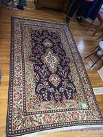 Full view of the large Persian style rug showing its intricate floral patterns and bordered design on a wooden floor.