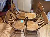 Four rustic solid wood dining chairs arranged in a square formation showing the seating surfaces and seat backs with country style vertical spindles.