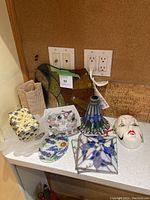 Photo of various decorative glass and ceramic items on a countertop including stained glass pieces and ceramic mask.