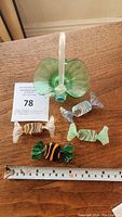Green Murano glass basket with clear handle and five candy shaped figurines of various colors and designs on wooden surface with measuring tape.