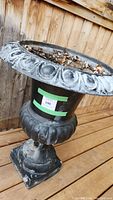 Side angle view of vintage planter showing ornate rim and pedestal base, planter filled with leaves and dirt