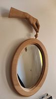 Mirror hanging on the wall showing the carved wooden hand and oval mirror frame.