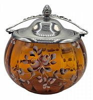 Front view of amber glass biscuit barrel showing hand painted floral design and silver plate lid with decorative finial.