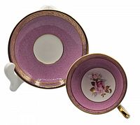 Top view of saucer and cup showing pink textured background, gold rim, and floral rose design inside cup
