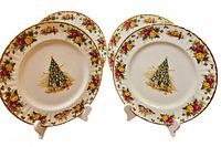 Pair of dinner plates displayed upright showing Christmas tree design in center, floral rose border, scalloped edges with gold trim