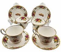 Four vintage Royal Albert tea cups and saucers with Old Country Roses Christmas Magic pattern displayed on stands showing floral and holiday themed designs with gold trim.