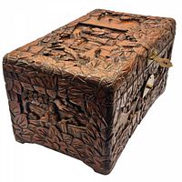 Angled view showing carved scenes of people and village life surrounded by carved flowers on a wooden box.