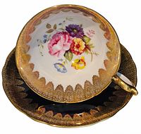 Vintage Aynsley cup and saucer set displayed. Cup shows floral pattern inside with gold rim, and matching saucer with gold and black details.