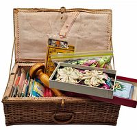 Open woven wicker sewing box showing satin and silk appliques, yarn, ribbons, and sewing supplies inside.