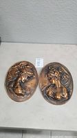 Pair of vintage cast iron oval plaques displayed side by side on a table, showing front profiles of two different young ladies.
