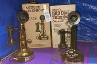 Photo showing two Beam antique telephone replicas with original packaging boxes against a blue backdrop, highlighting the brass finish phone on the left and black finish phone on the right alongside the decanter box.