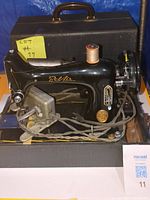 Full view of Bel Air Bantam Sewing Machine with foot pedal and braided electrical cord in front of a black carrying case with handle.