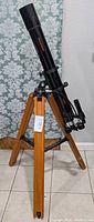 Full view of Celestron Premium 80 refractor telescope mounted on wooden tripod against a patterned backdrop.