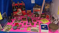 Overview of lot including Coca Cola bottles, Wolo train horn box, pins, keychains, stamps, and large glass